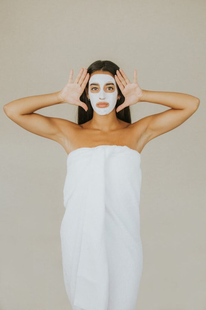 Woman wearing a white face mask and towel in a studio setting, promoting skincare and relaxation.