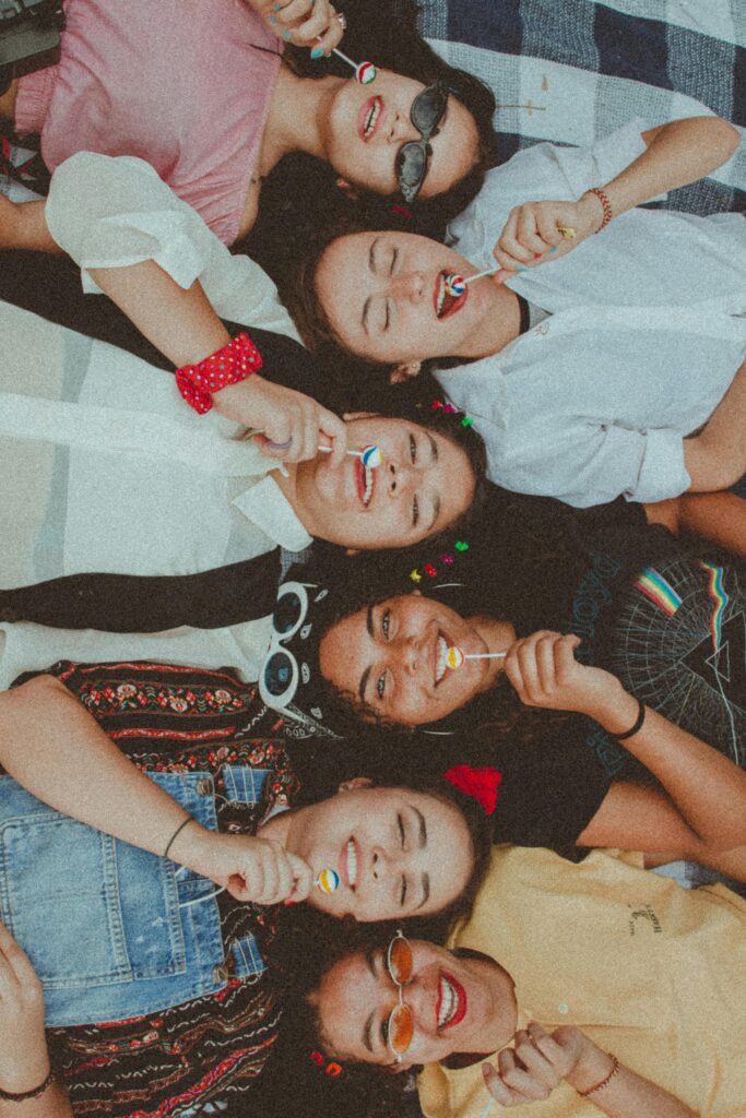 Joyful group of diverse women enjoying a sunny picnic with lollipops, showcasing friendship and fun.