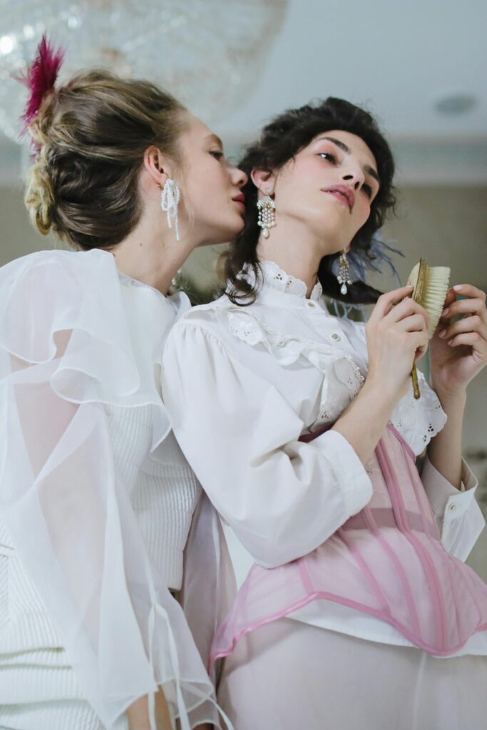 Two women in Victorian-inspired attire share a moment in a classic setting.